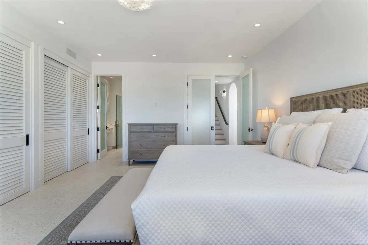 A bright bedroom with a bed, bedside lamp, and dresser.