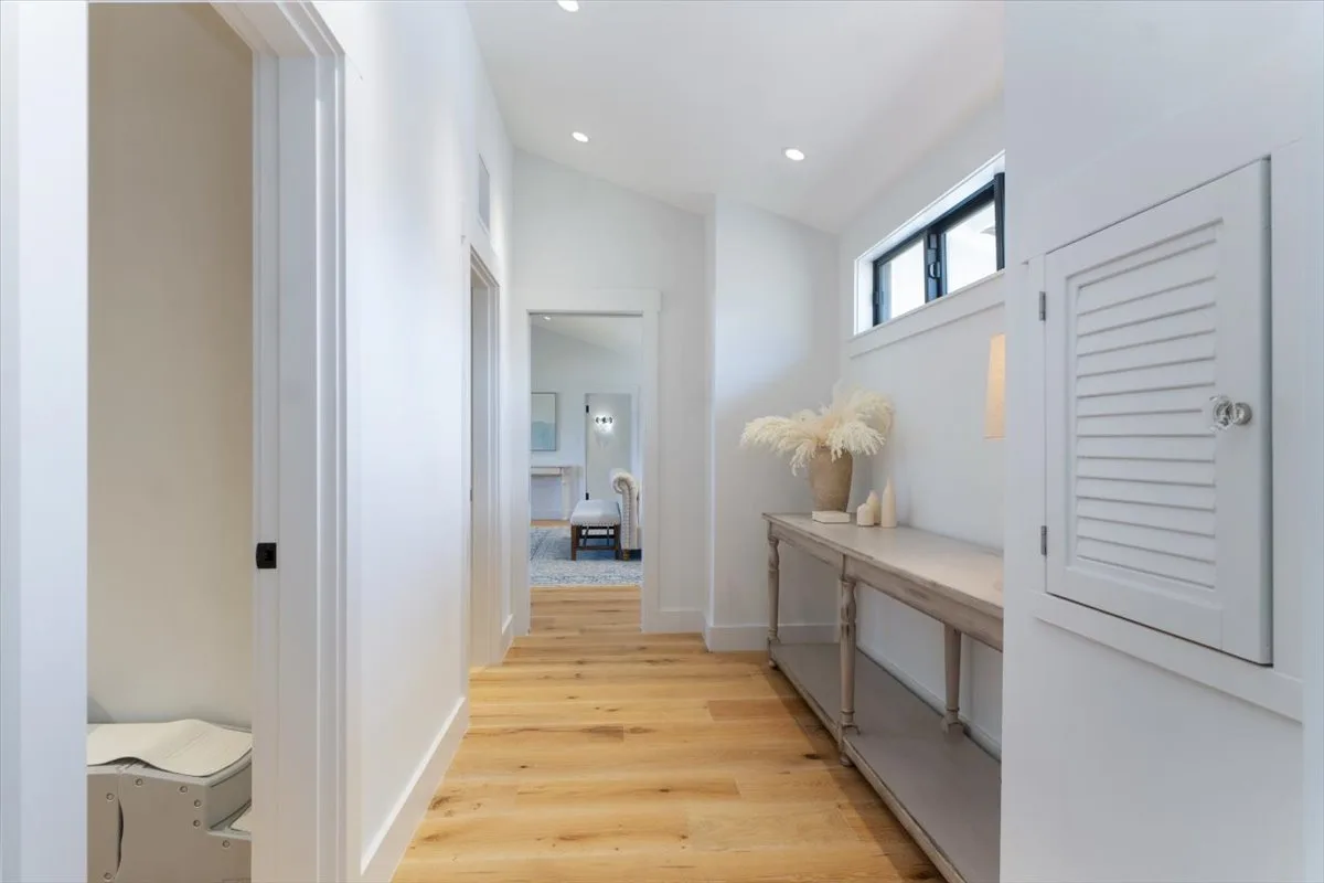 A bright hallway with wood flooring, a console table, and a doorway at the far end.