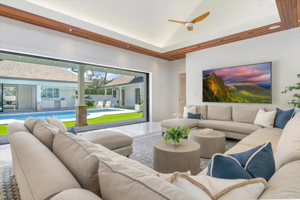 A bright living room with seating around a coffee table and a large window overlooking a pool.