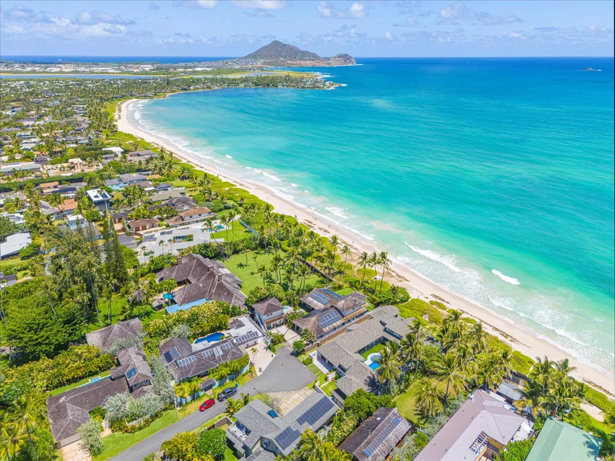 An aerial view of a coastal neighborhood beside a sweeping beach and turquoise sea.