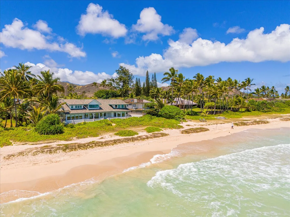 A beachfront property borders a sandy shore with palm trees and ocean waves.