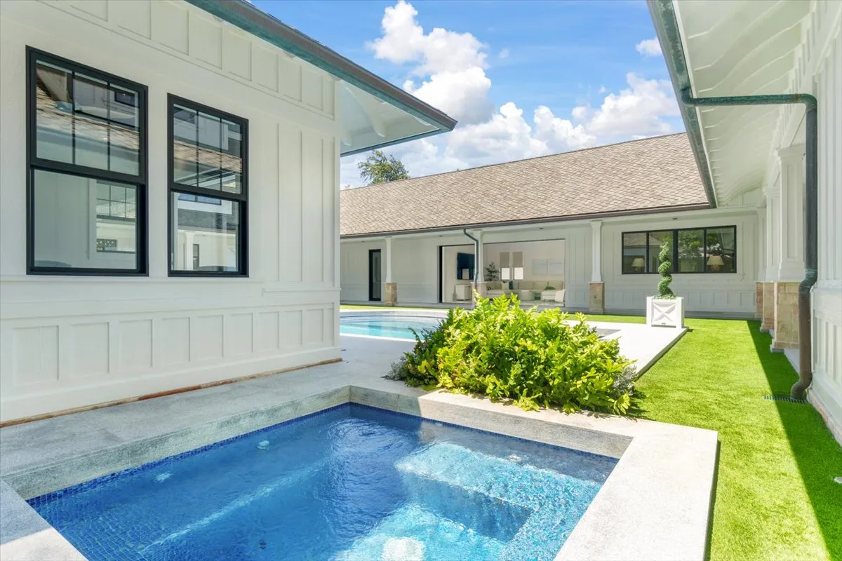 A courtyard pool sits beside white buildings, with green lawn and shrubs.