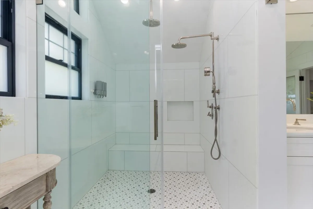 A bright tiled bathroom with a glass shower and a window.