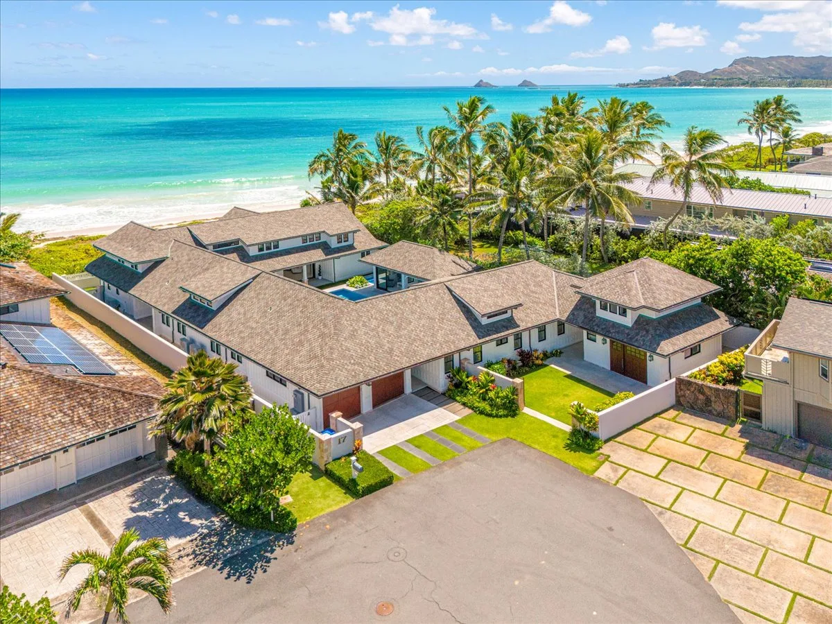 Aerial view of a coastal property beside a turquoise beach and palm trees.