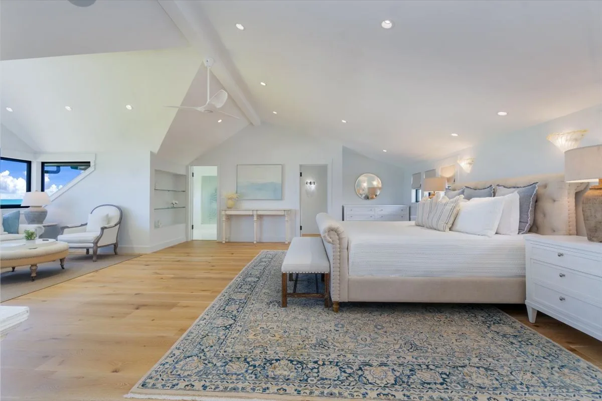 A bright bedroom with a large bed, a patterned rug, and a small seating area.