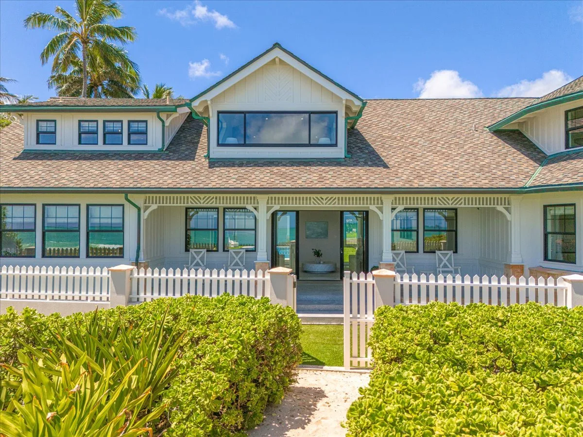 A house exterior with a covered porch, white fence, and green hedges.