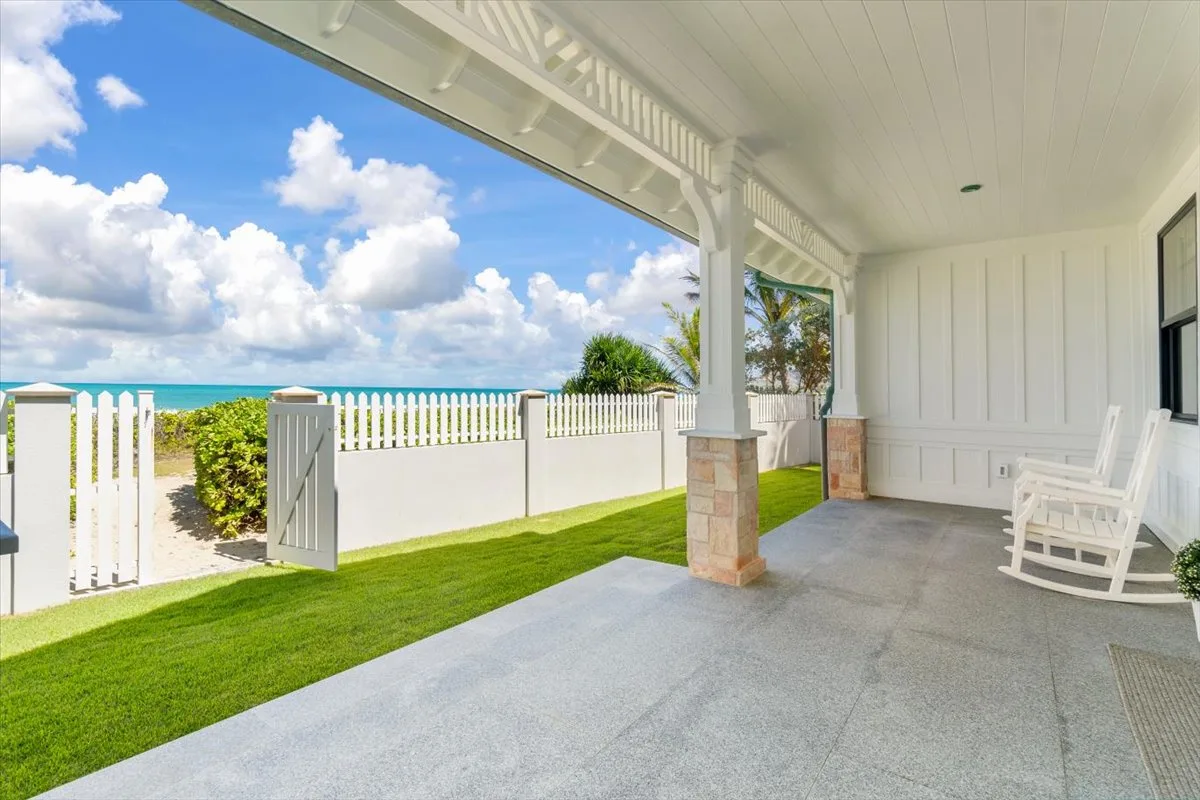 A covered patio overlooks a fenced lawn and the ocean.