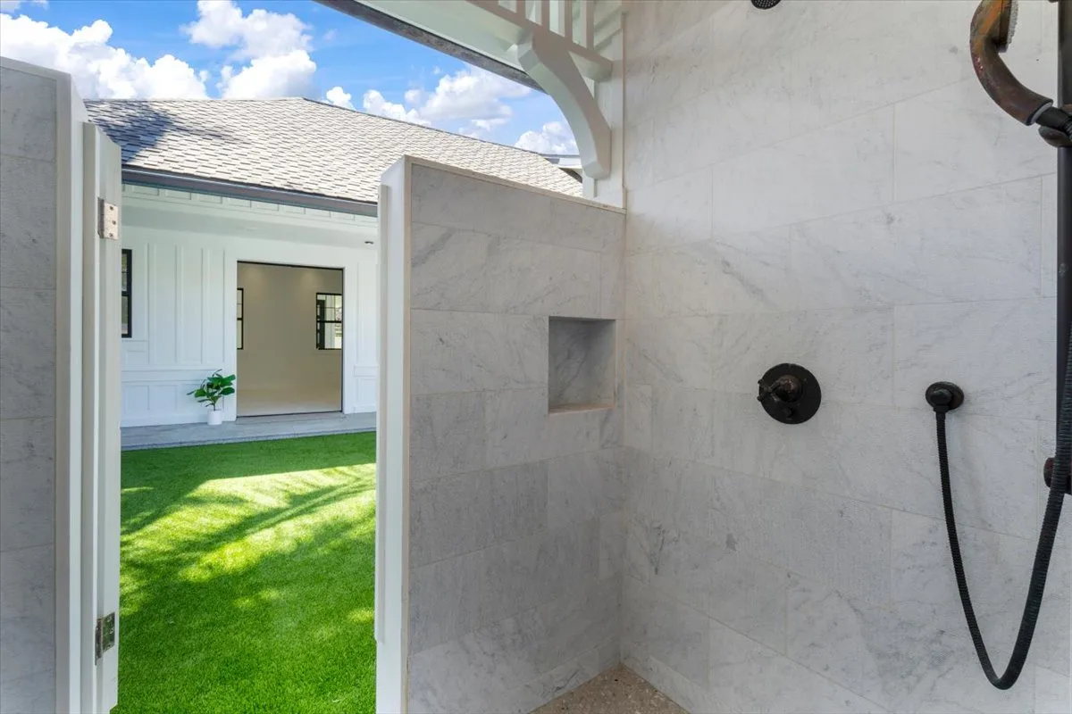 An outdoor shower opens onto a grassy yard and a white building.