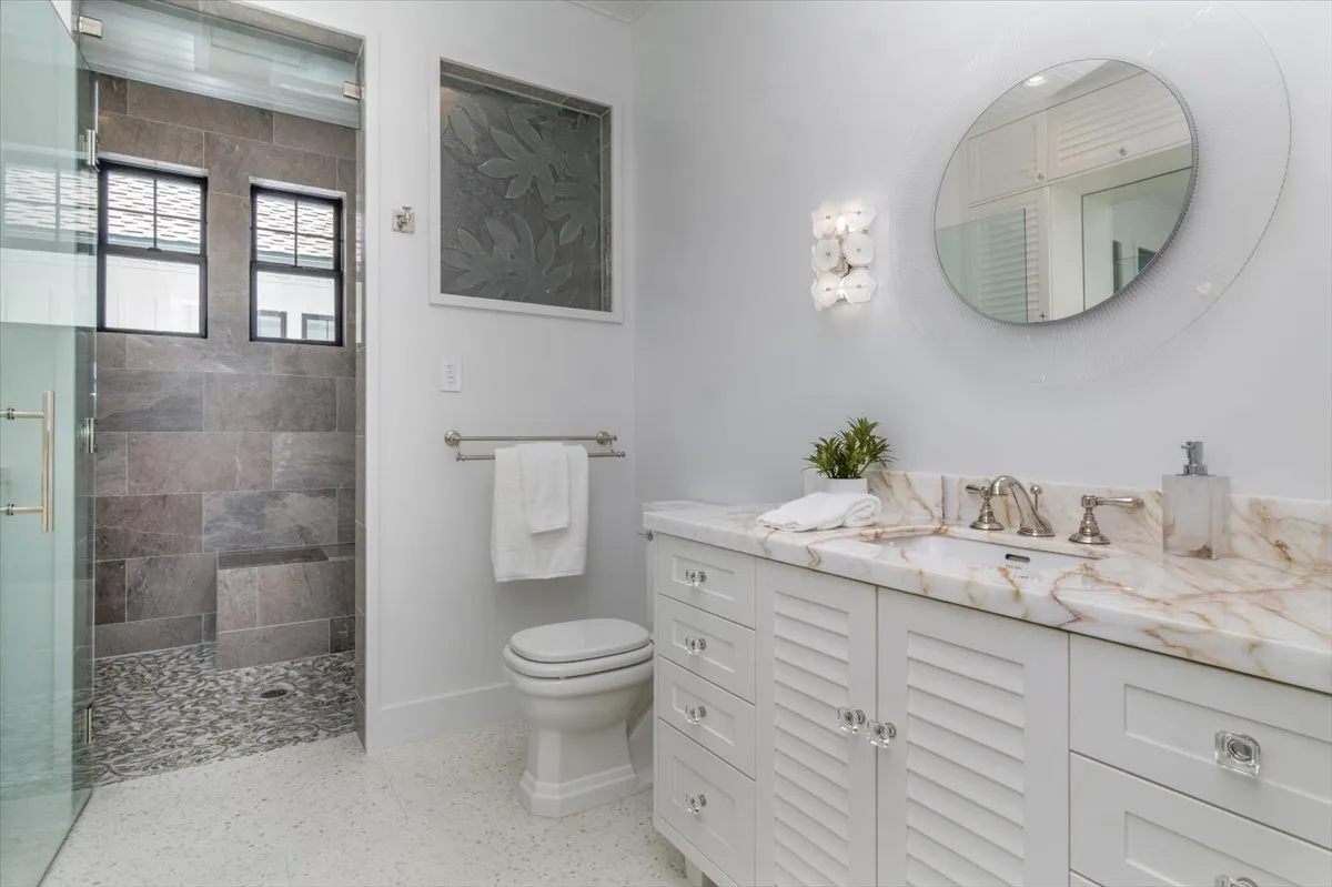 A bright bathroom with a long vanity, round mirror, and glass shower.