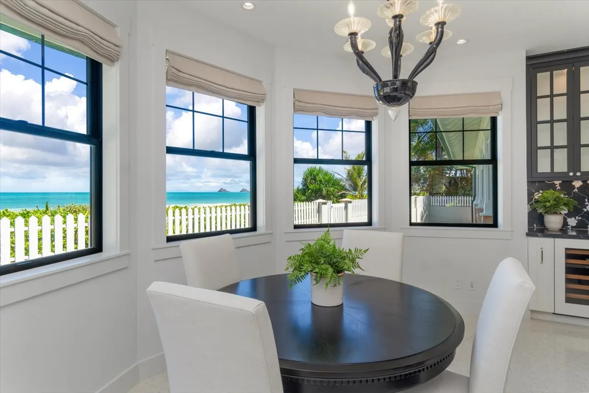 A bright dining area has a round table beside large windows overlooking the water.
