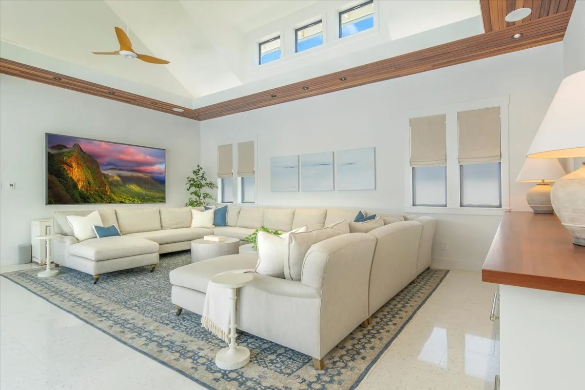 A bright living room with seating arranged around a coffee table beneath high windows.