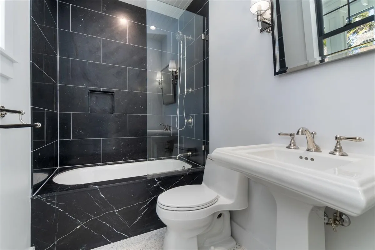 A bathroom with a bathtub behind a glass shower screen and a pedestal sink.