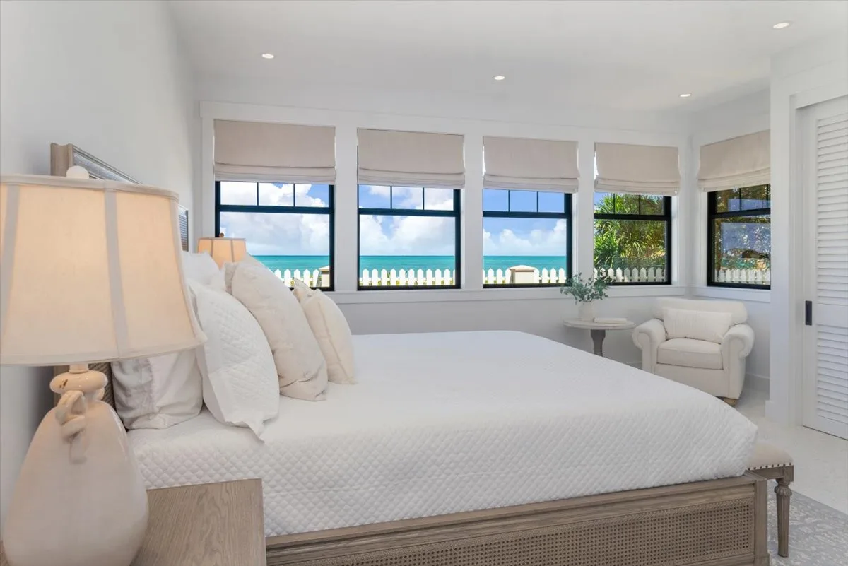 A bright bedroom with a large bed and windows overlooking the water.