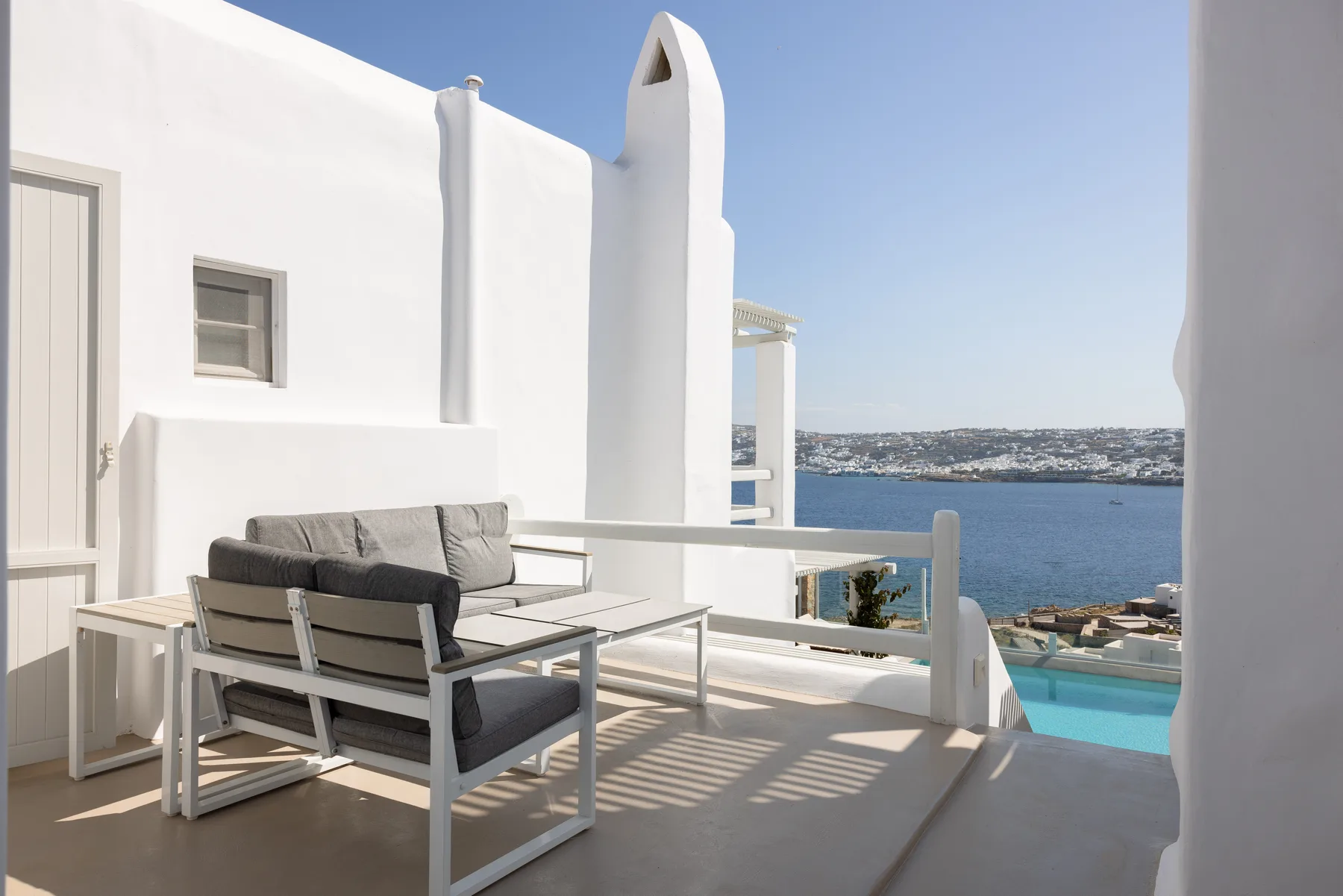 A sunny terrace with outdoor seating overlooks the sea and a swimming pool.