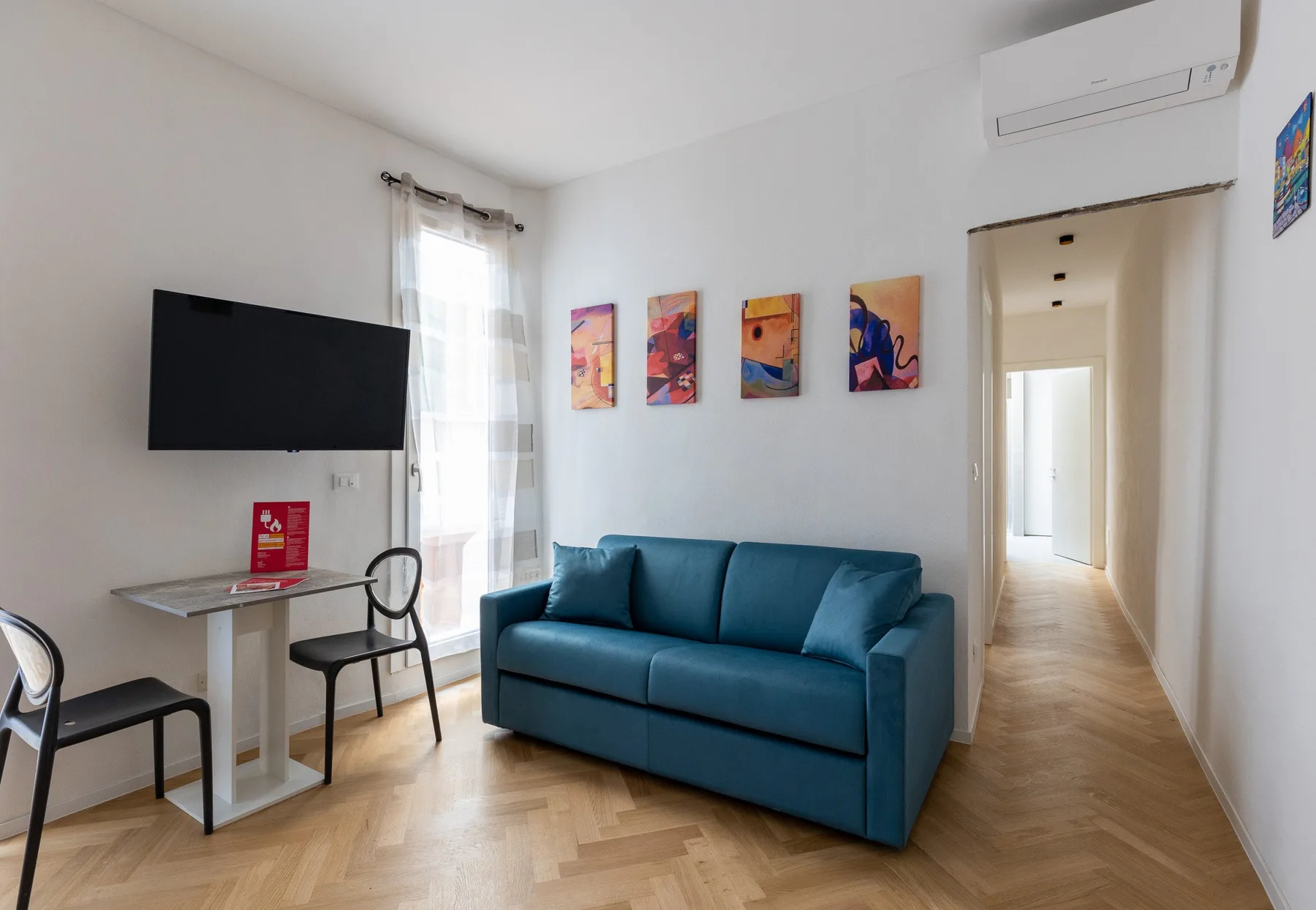 A bright living room with blue seating, a television, and colorful wall art.