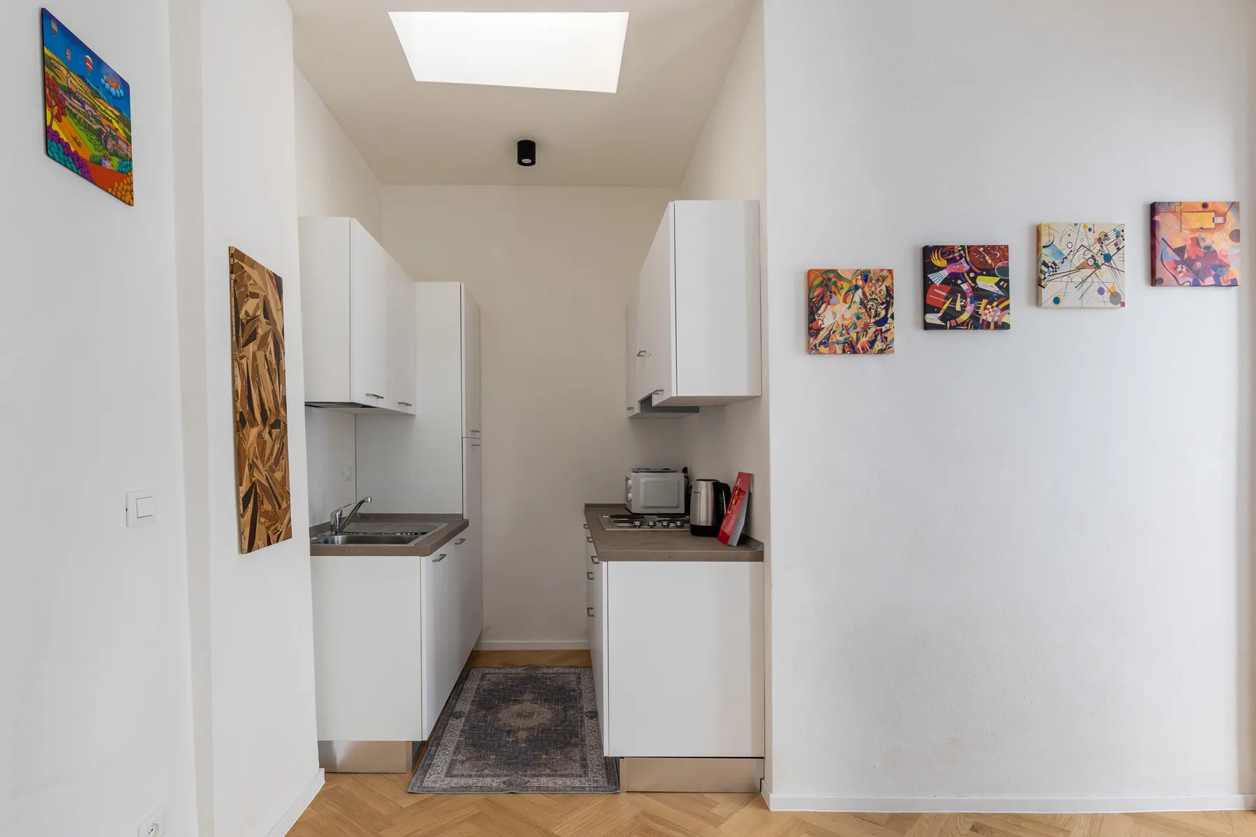 A compact kitchen with white cabinets, a counter, and colorful wall art.