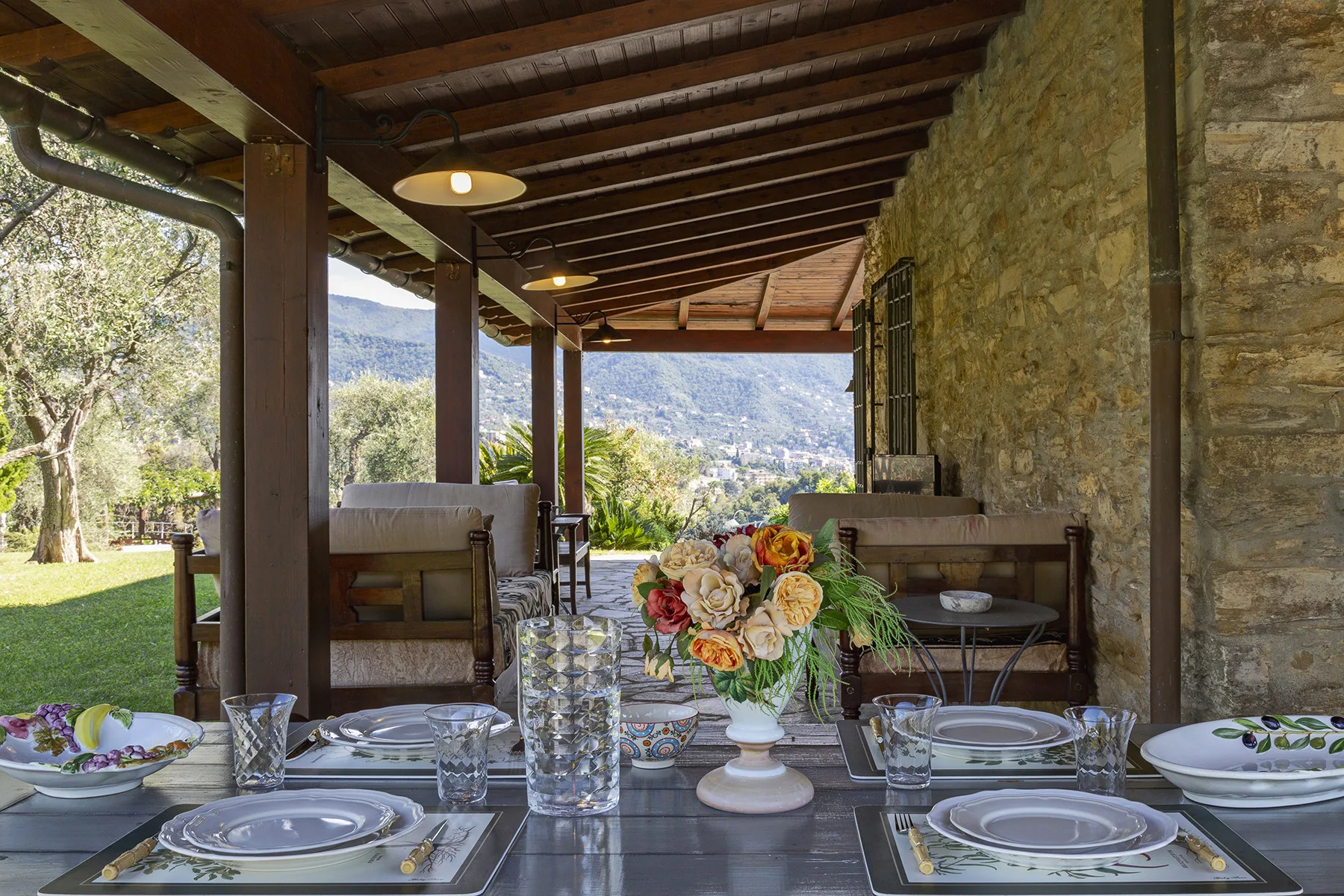 Comedor exterior cubierto con una mesa puesta y vistas a una ladera verde.