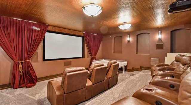 A home theater with a large projection screen, red curtains, and rows of seating.