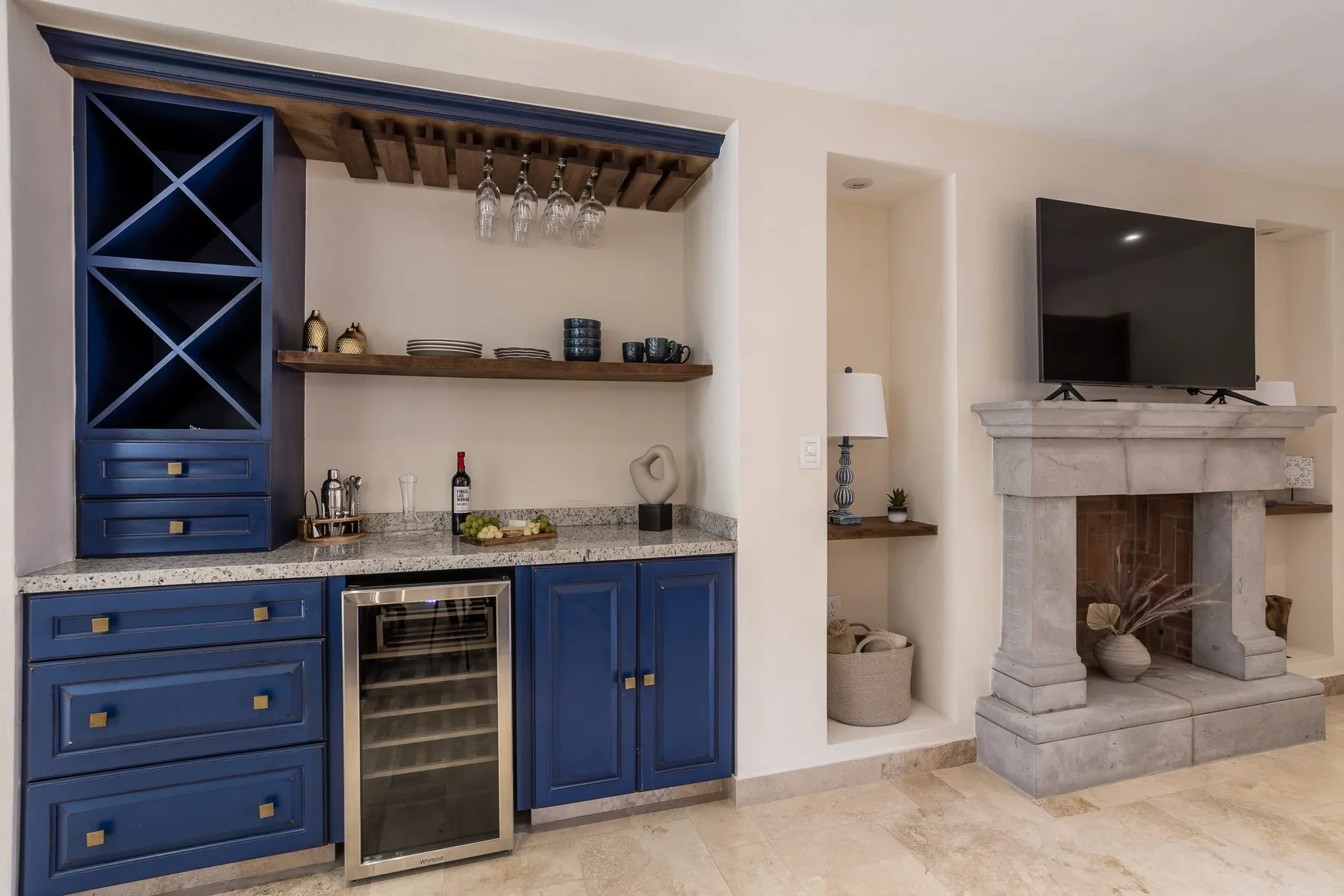 Una sala de estar con una barra empotrada azul junto a una chimenea de piedra y un televisor.