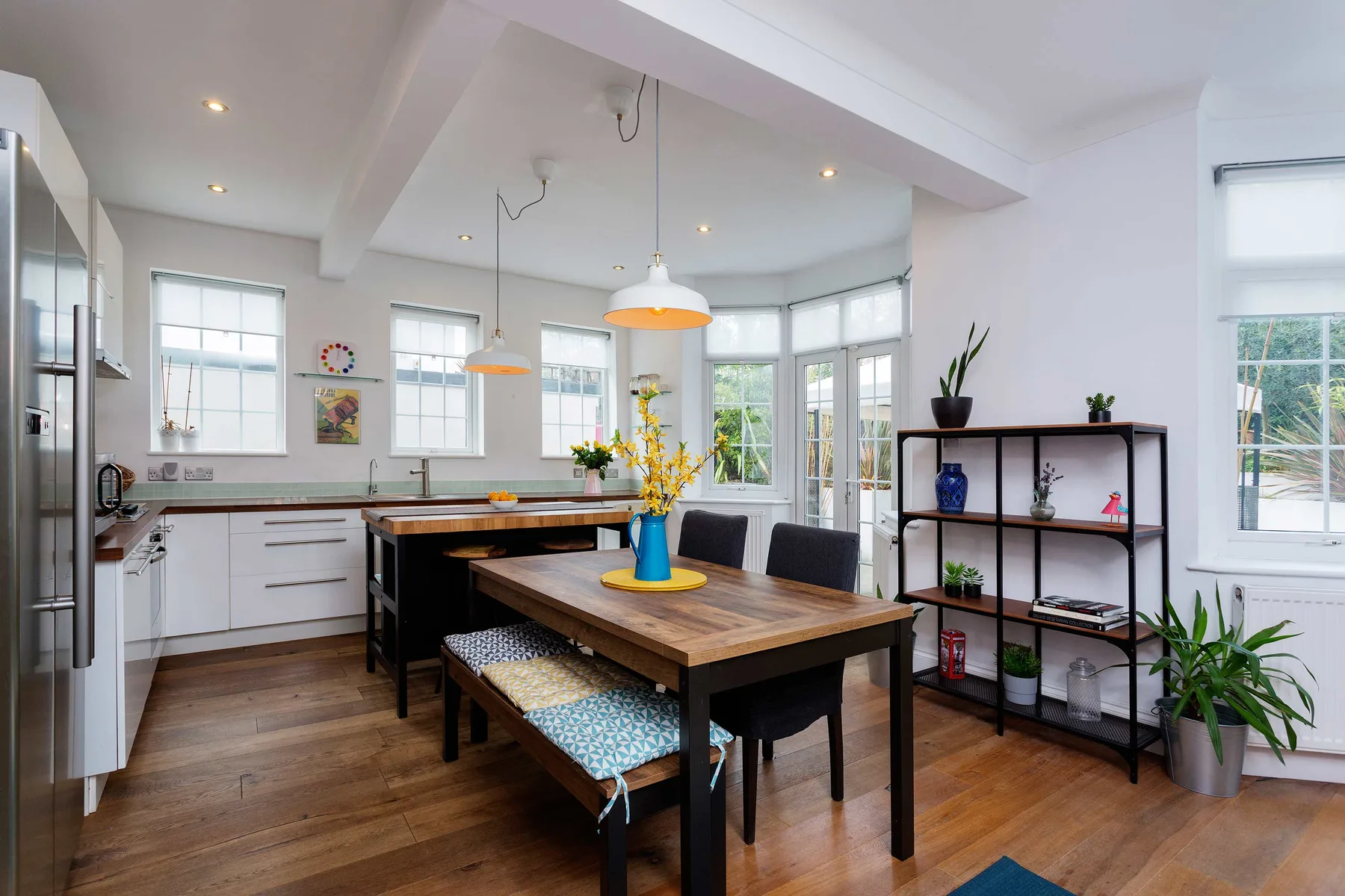 Un comedor luminoso con una mesa de madera junto a la cocina y ventanas grandes.