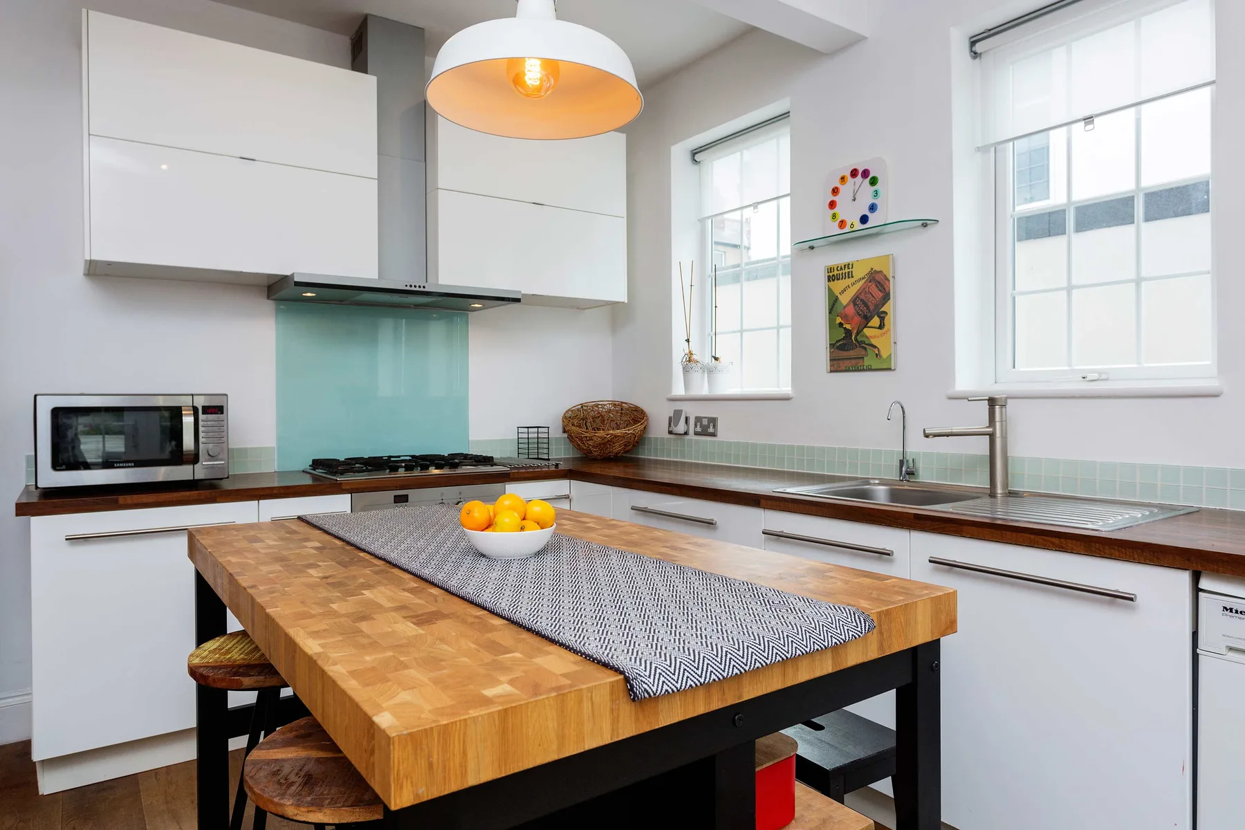 Una cocina luminosa con gabinetes blancos, salpicadero de azulejos e isla de madera.