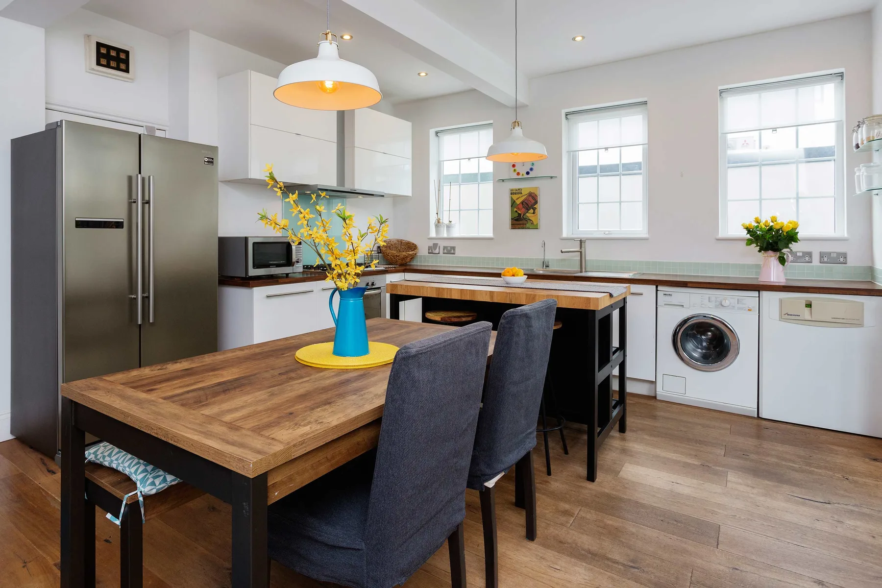 Una cocina luminosa con comedor cuenta con una gran mesa de madera bajo lámparas colgantes.