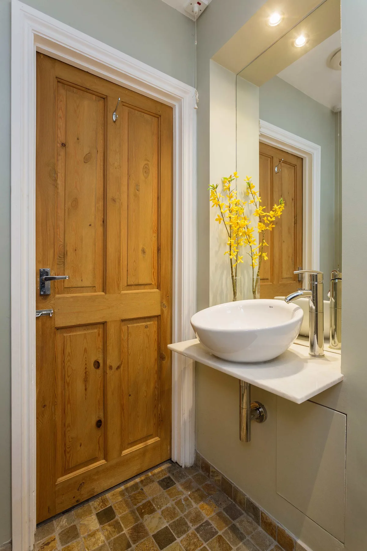 Un lavabo de baño con un lavamanos de sobremesa está junto a una puerta de madera.
