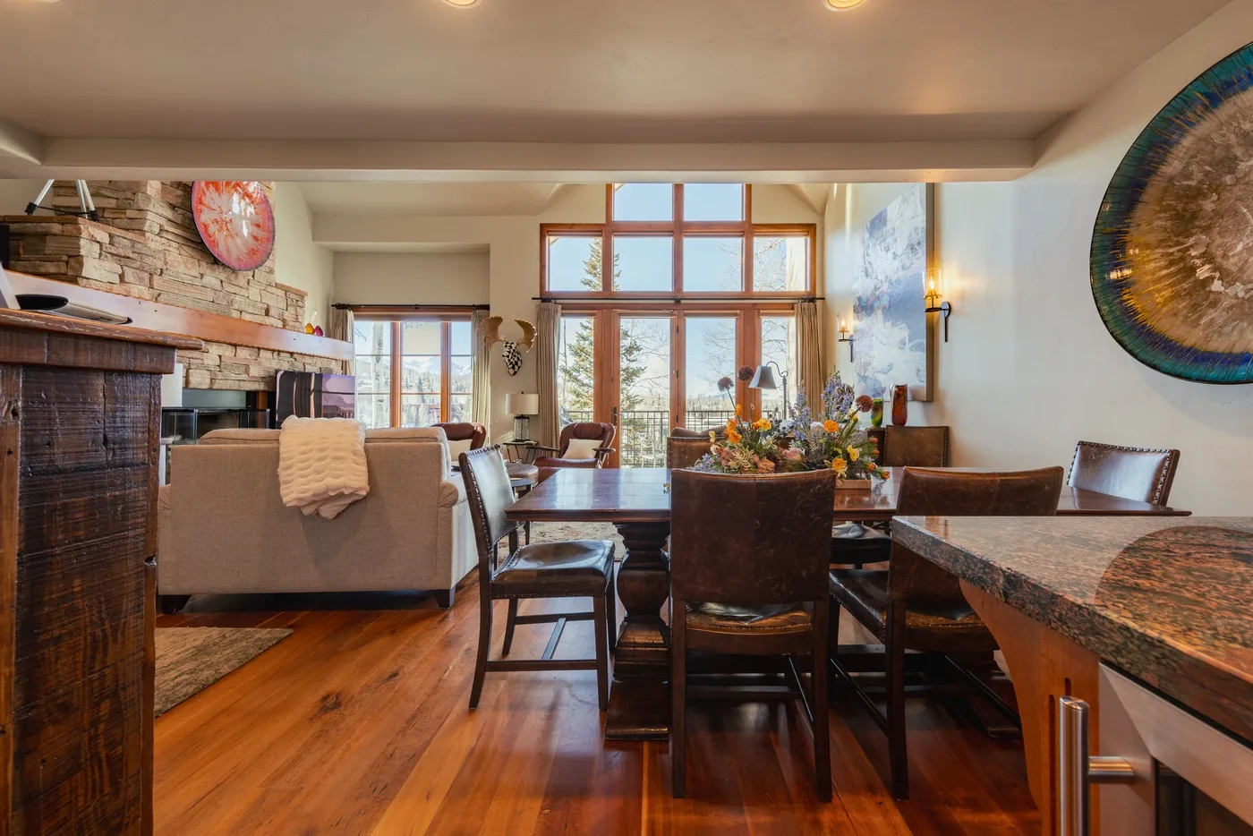 A dining area with a wooden table beside a living room and large windows.