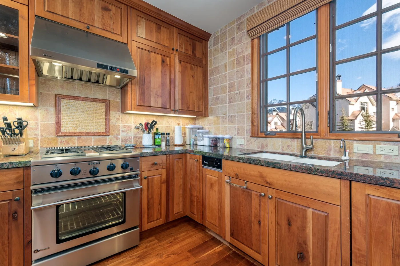 A wood-cabinet kitchen with a stainless steel range and large windows.