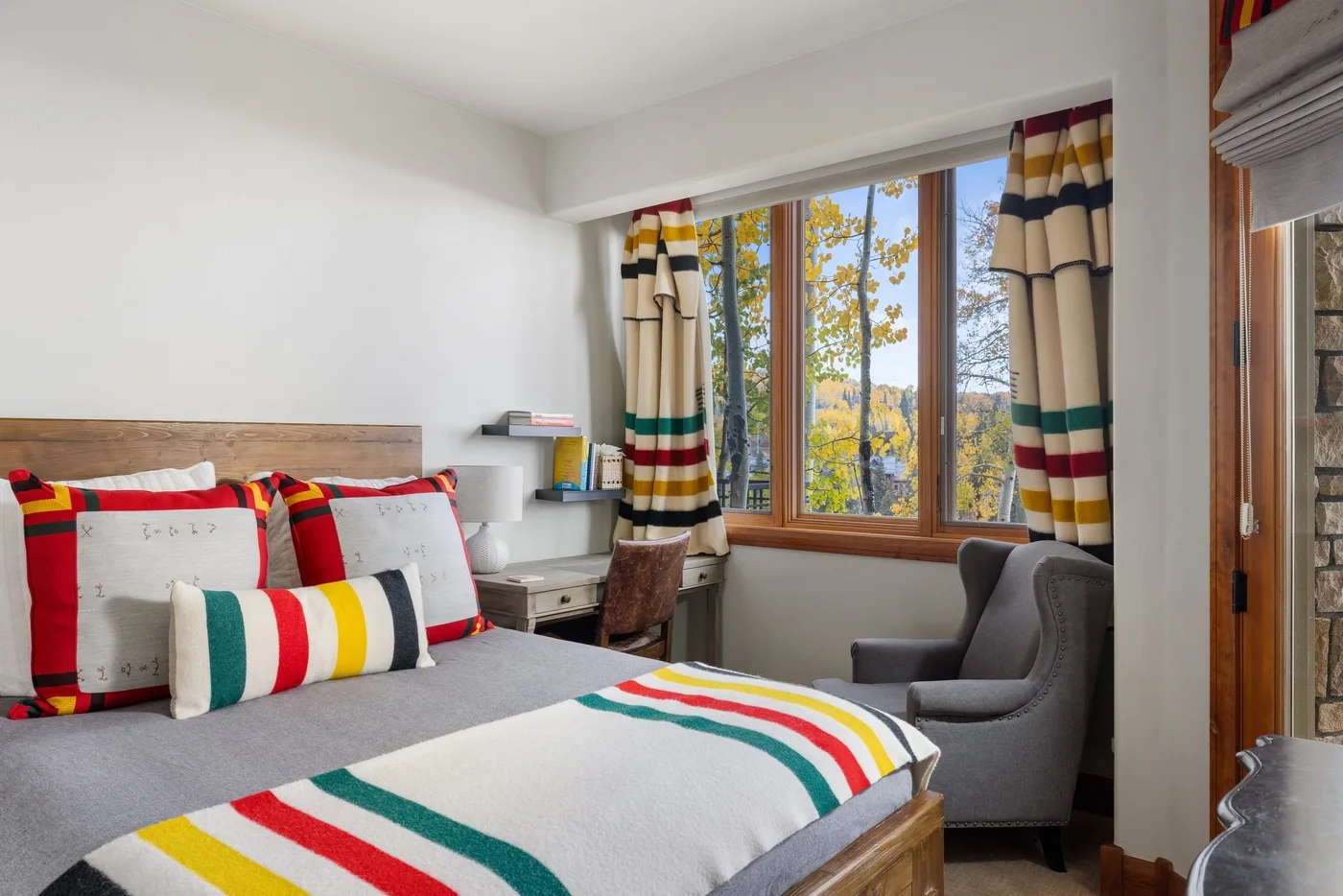 A bedroom with a bed dressed in colorful striped bedding beside a window.