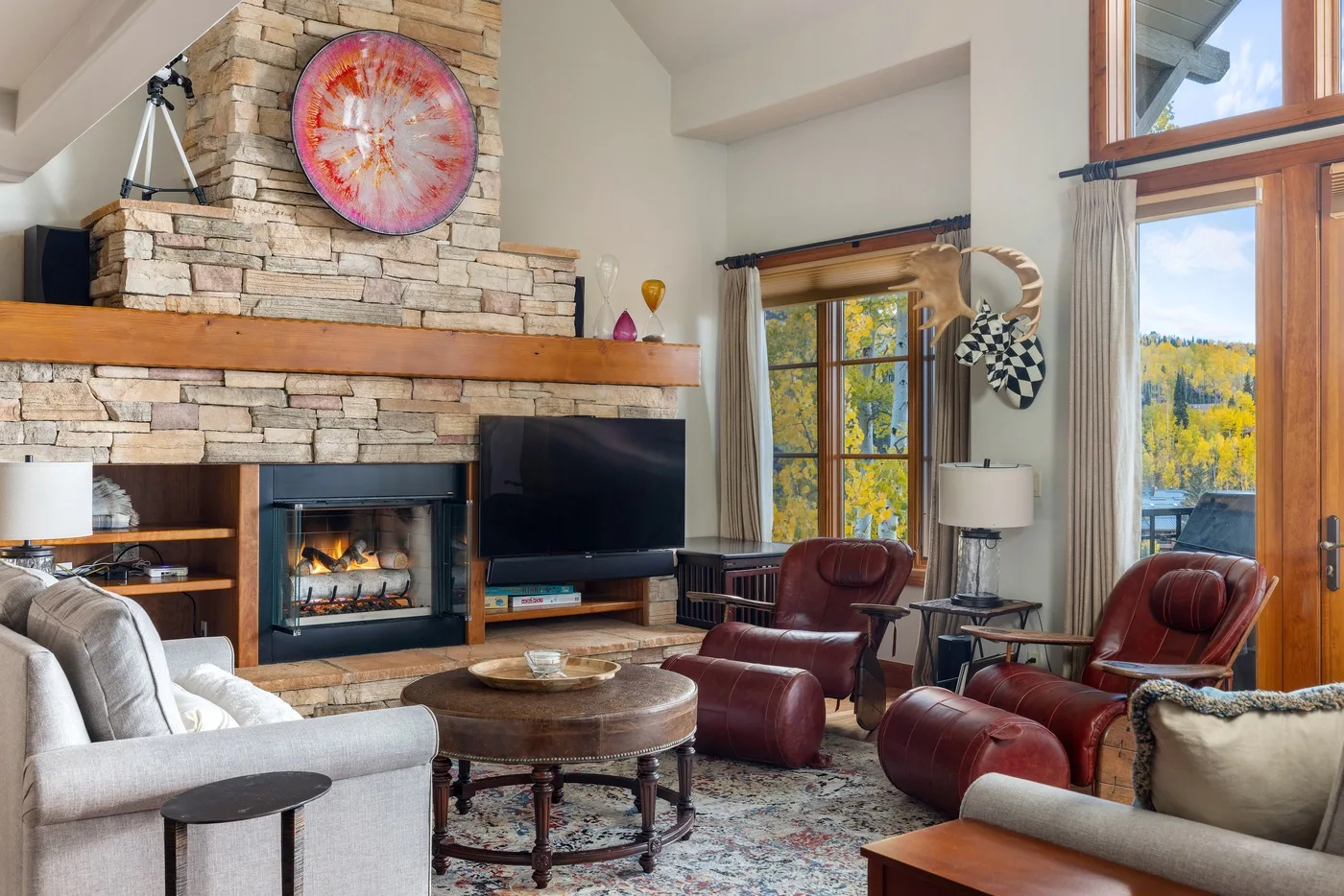 A living room with a stone fireplace, seating, and large windows.