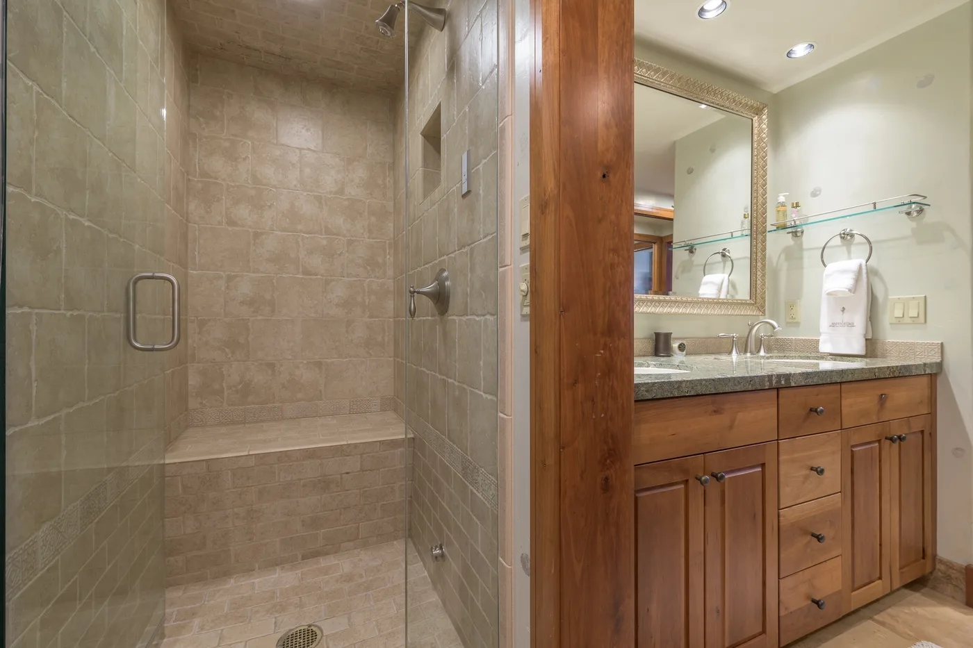 A tiled bathroom with a walk-in shower and a wooden vanity beside a mirror.