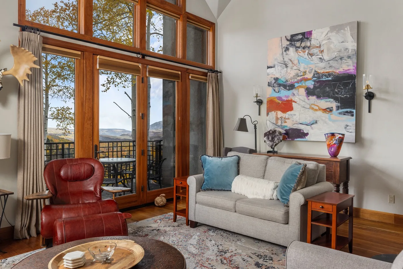A bright living room with large windows, seating, and colorful abstract artwork.