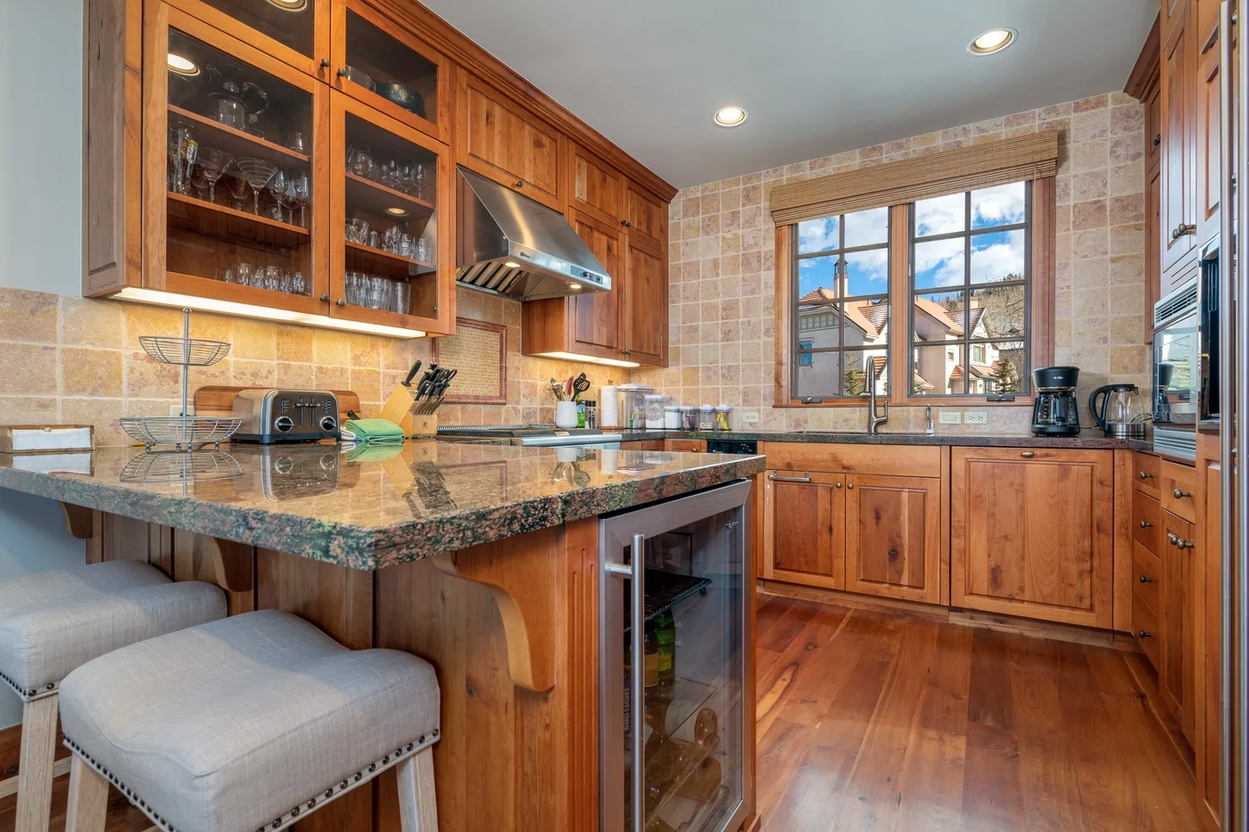 A warm wood kitchen with glass-front cabinets, a central island, and a window.