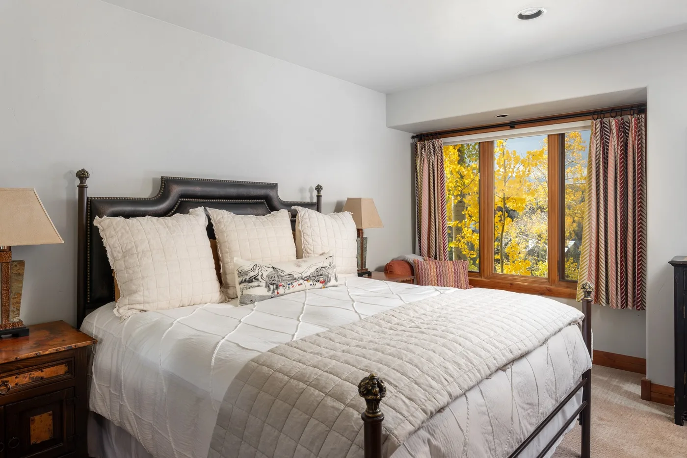 A bedroom with a large bed beside a window overlooking autumn-colored trees.