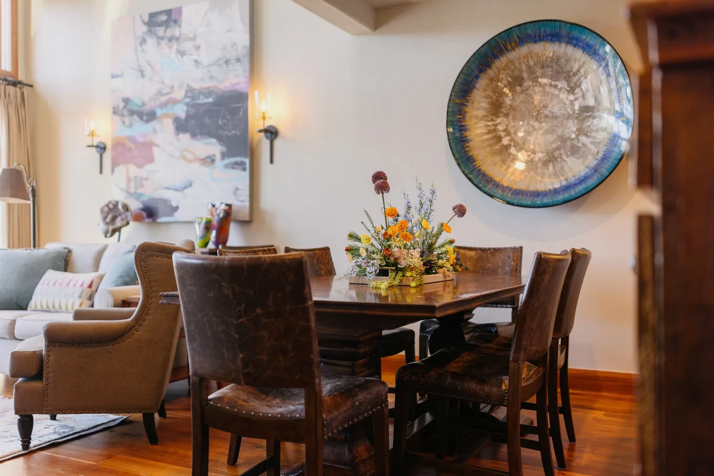 A dining area with a wooden table, upholstered seating, and colorful wall art.