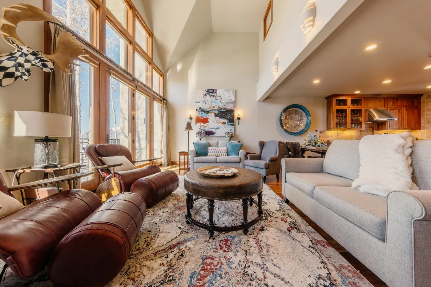 A bright living room with floor-to-ceiling windows and seating around a coffee table.