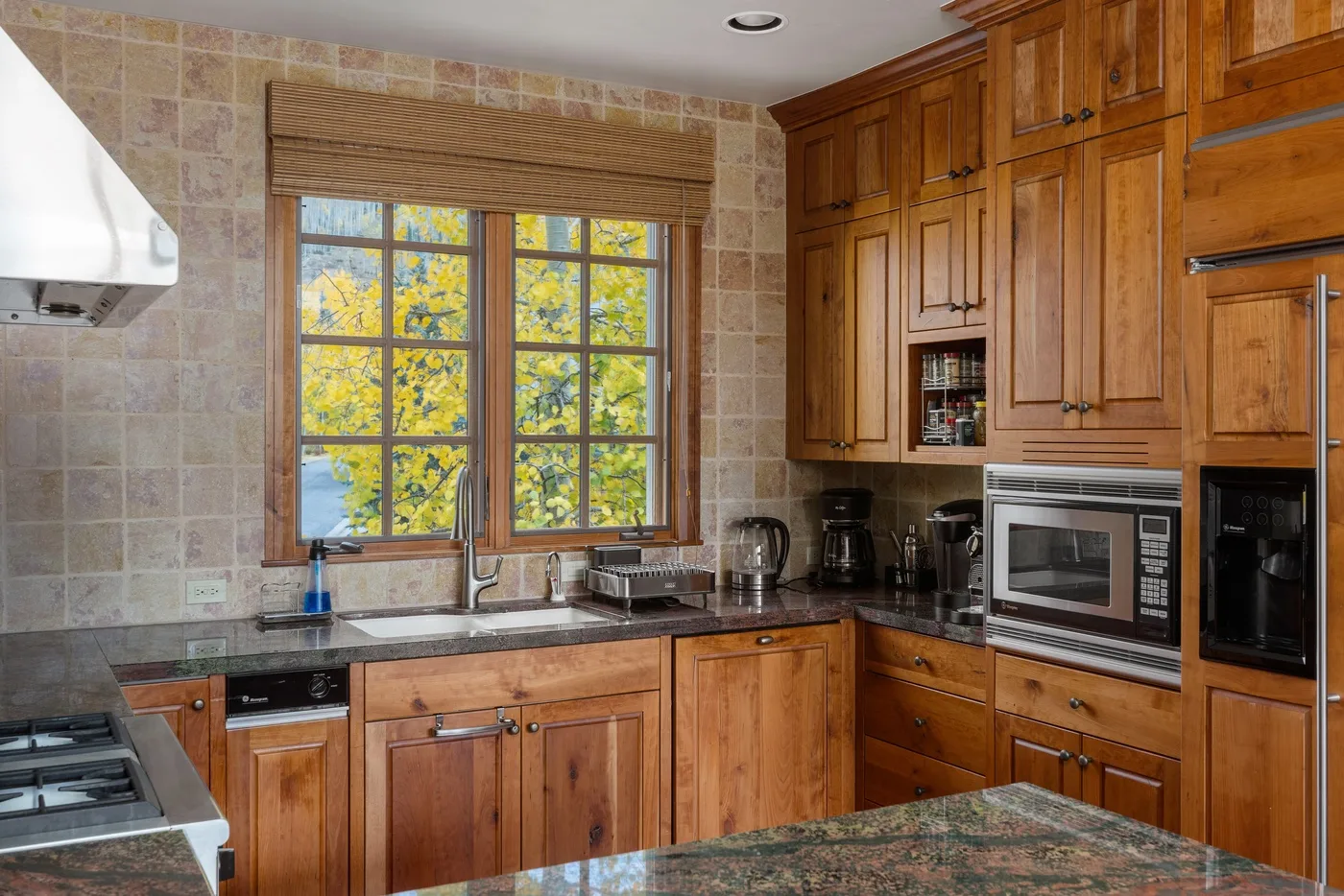 A kitchen with wooden cabinets, a sink, and a window overlooking trees.