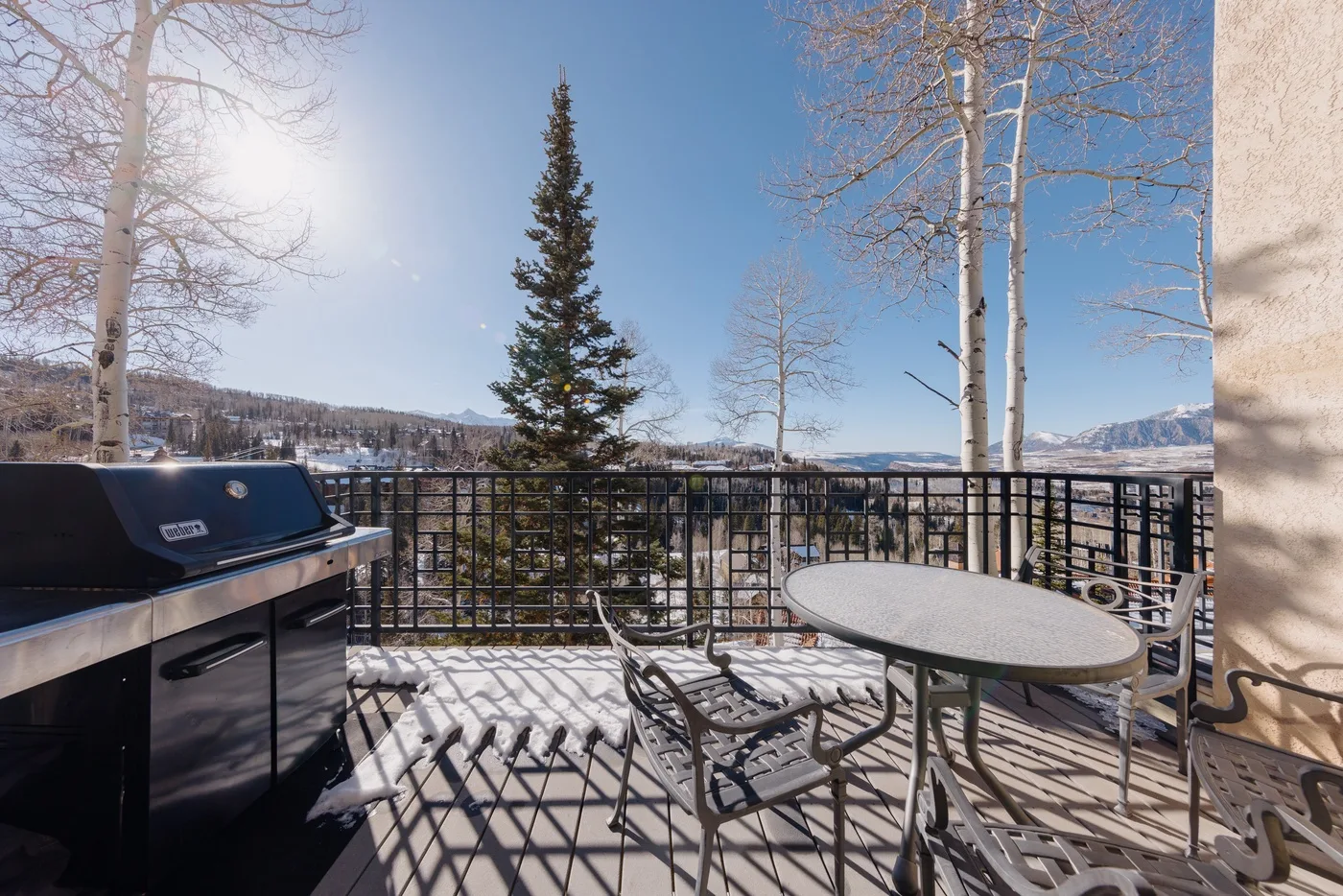A sunny outdoor deck has a grill, seating, and mountain views.