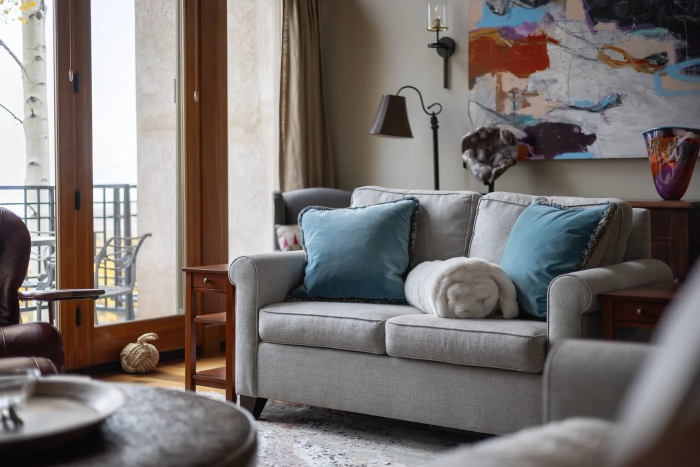 A living room with a gray sofa, blue cushions, and an abstract painting.