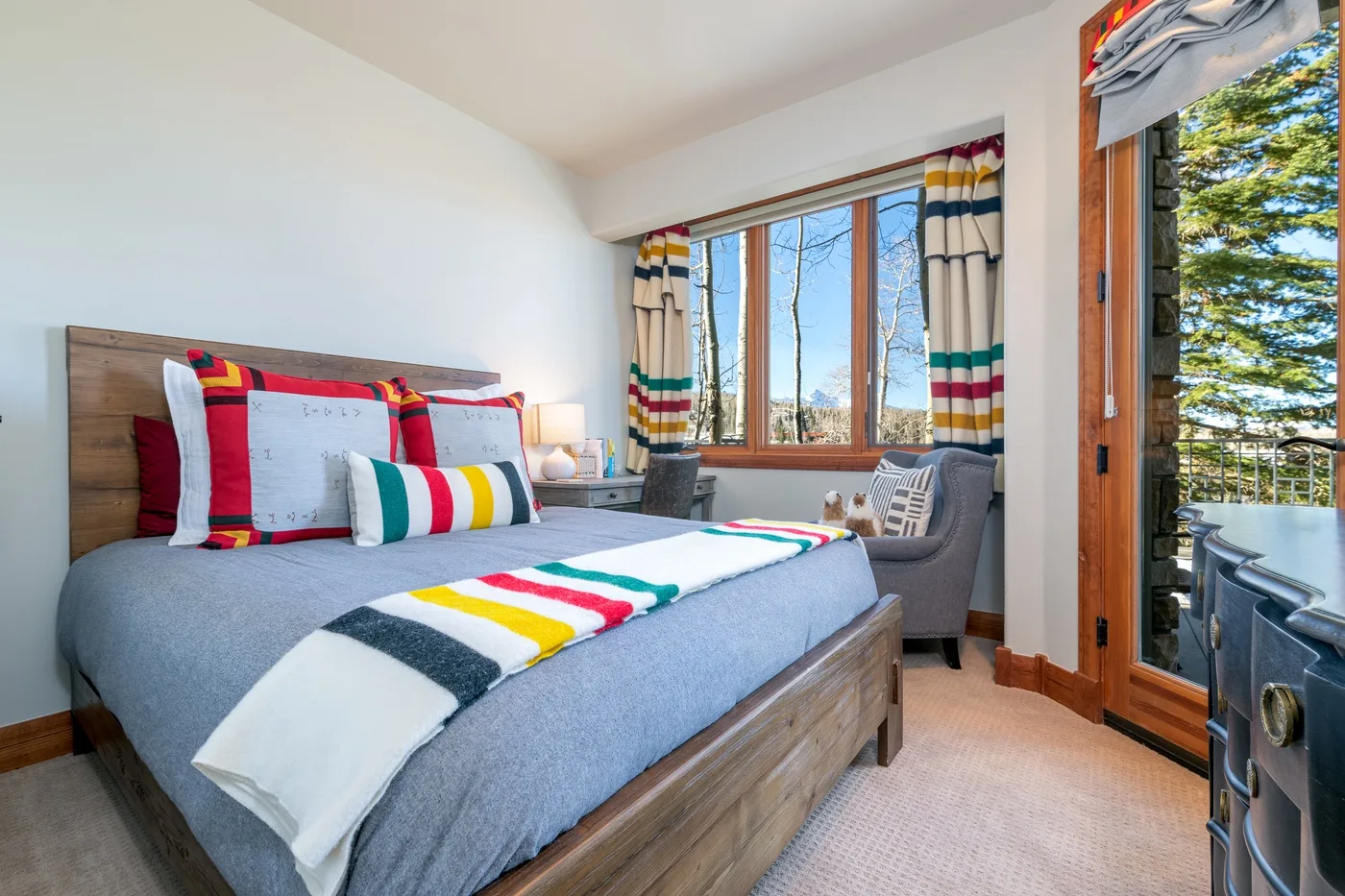 A bedroom with a bed dressed in colorful striped bedding beside a window.