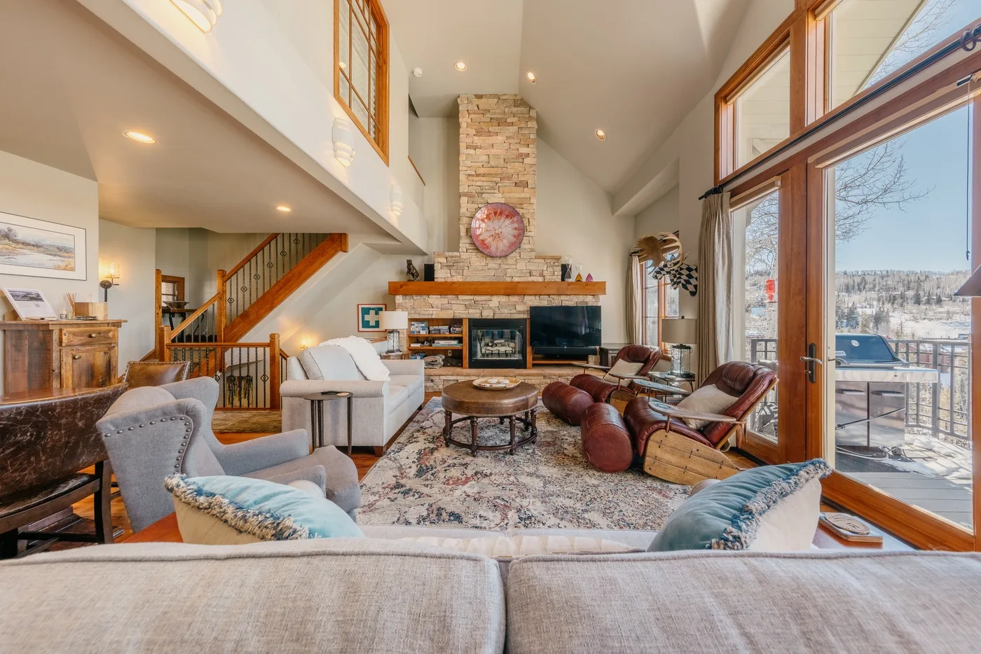 A spacious living room with seating arranged around a fireplace and large windows.