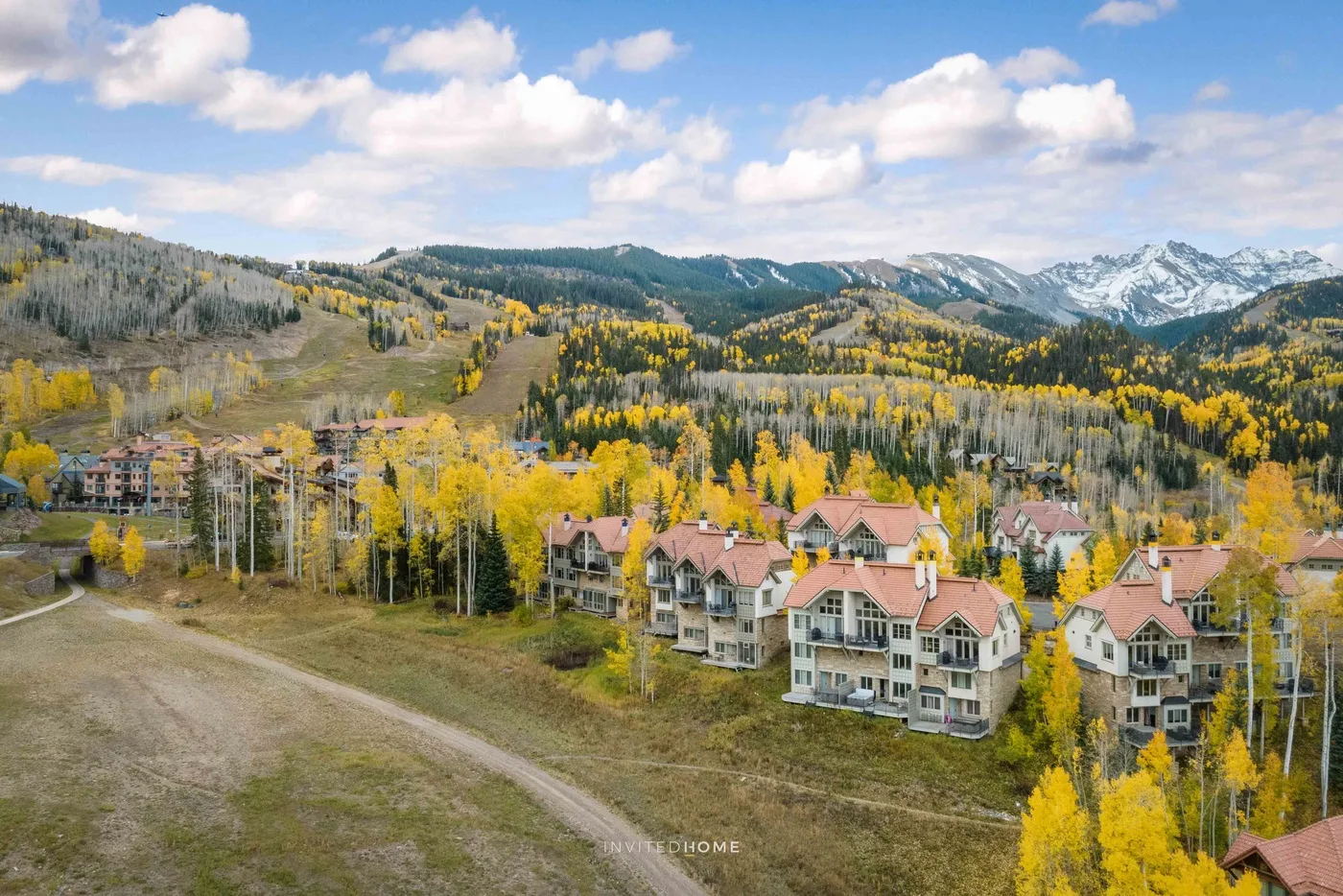 A mountain resort village sits among golden autumn trees beneath snow-dusted peaks.
