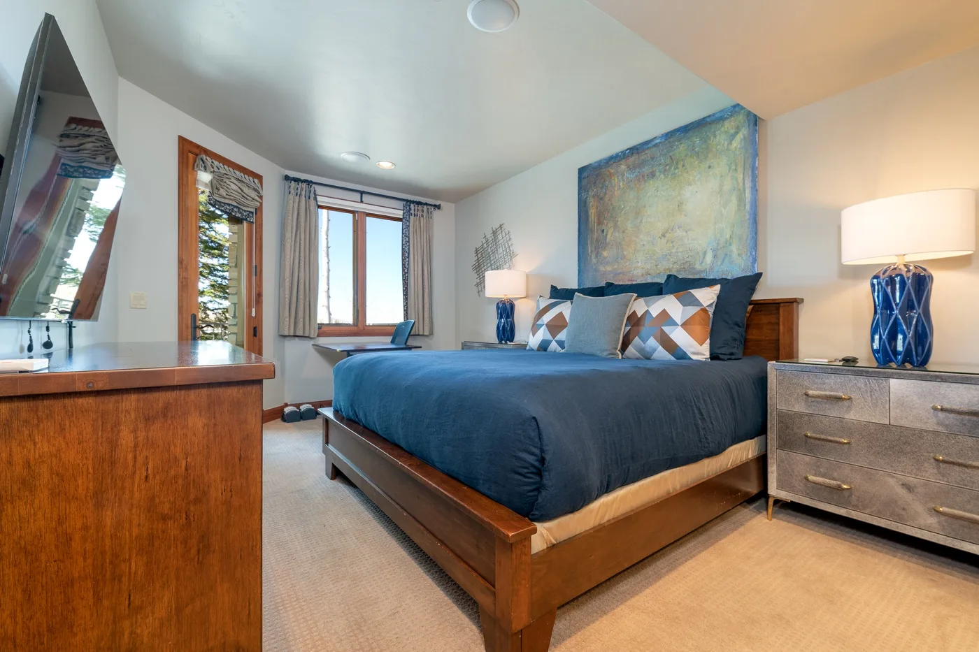 A bedroom with a bed, blue bedding, and a large painting above the headboard.