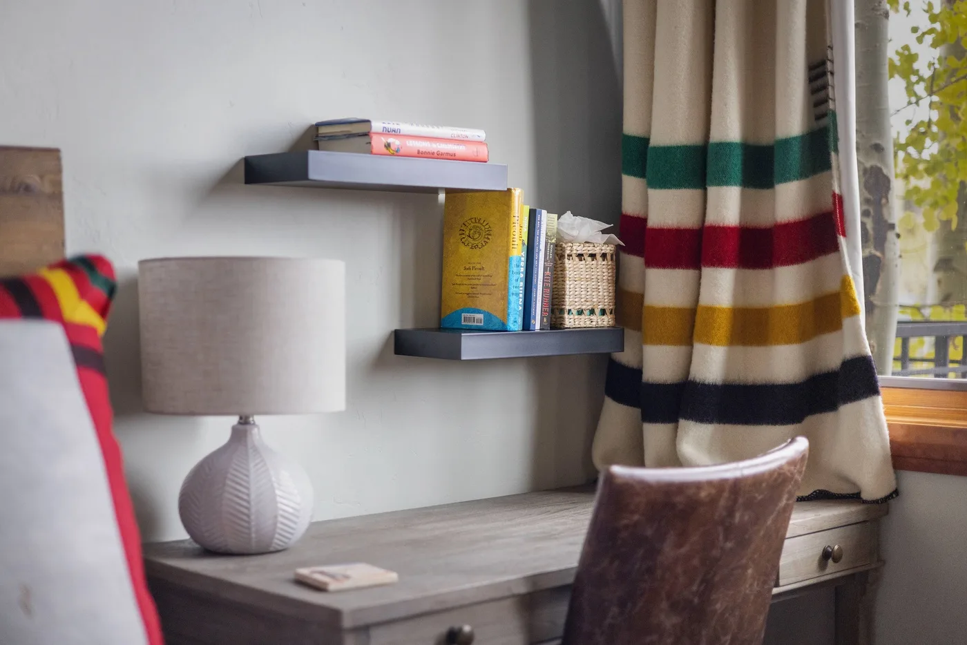 A desk sits beneath wall shelves beside striped curtains and a window.