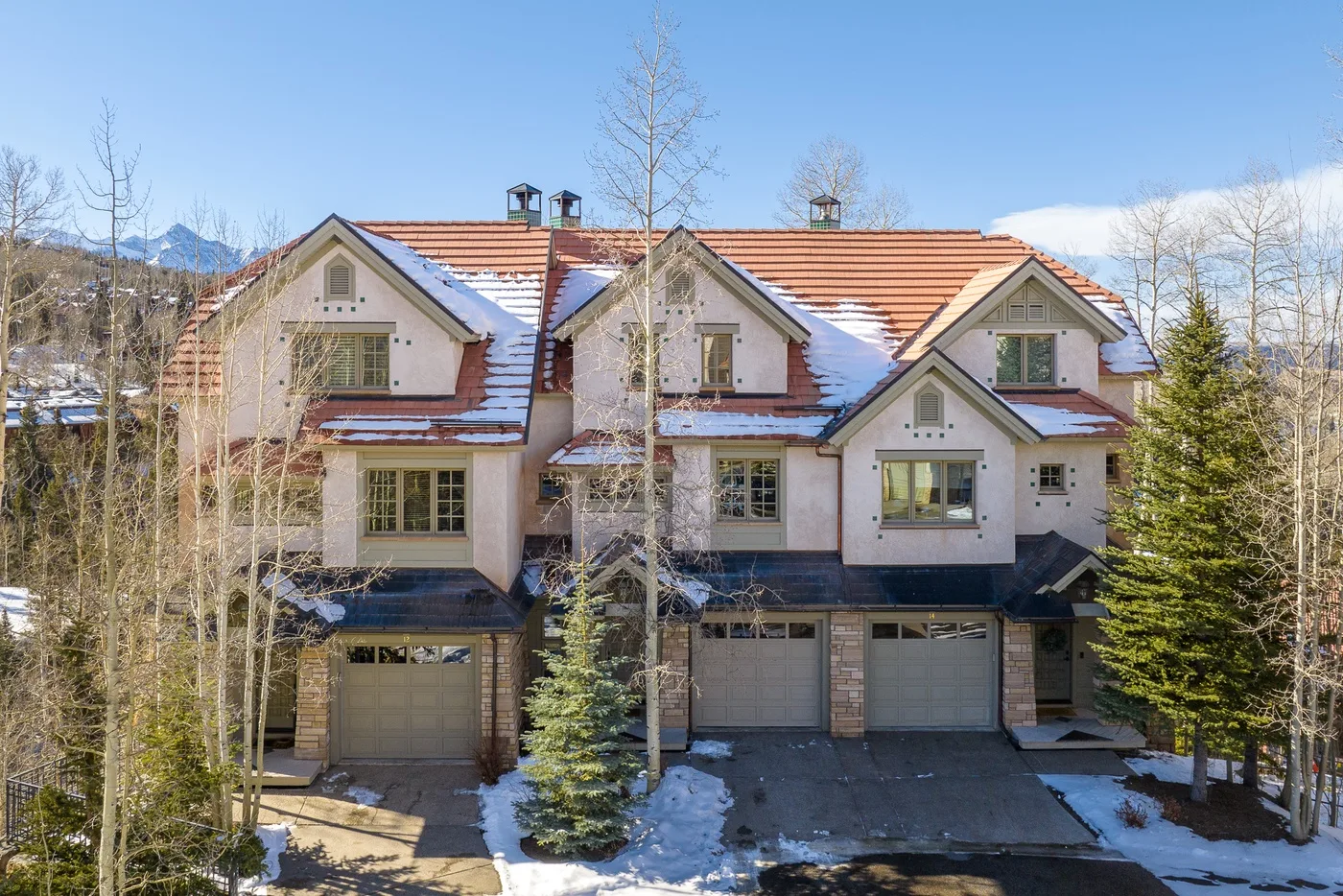 A row of attached homes with peaked roofs and garage doors, surrounded by trees.