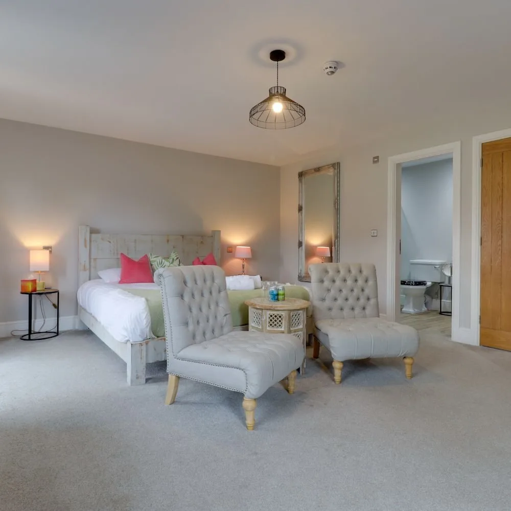 Spacious bedroom with two armchairs, a small table and an ensuite visible through the doorway.
