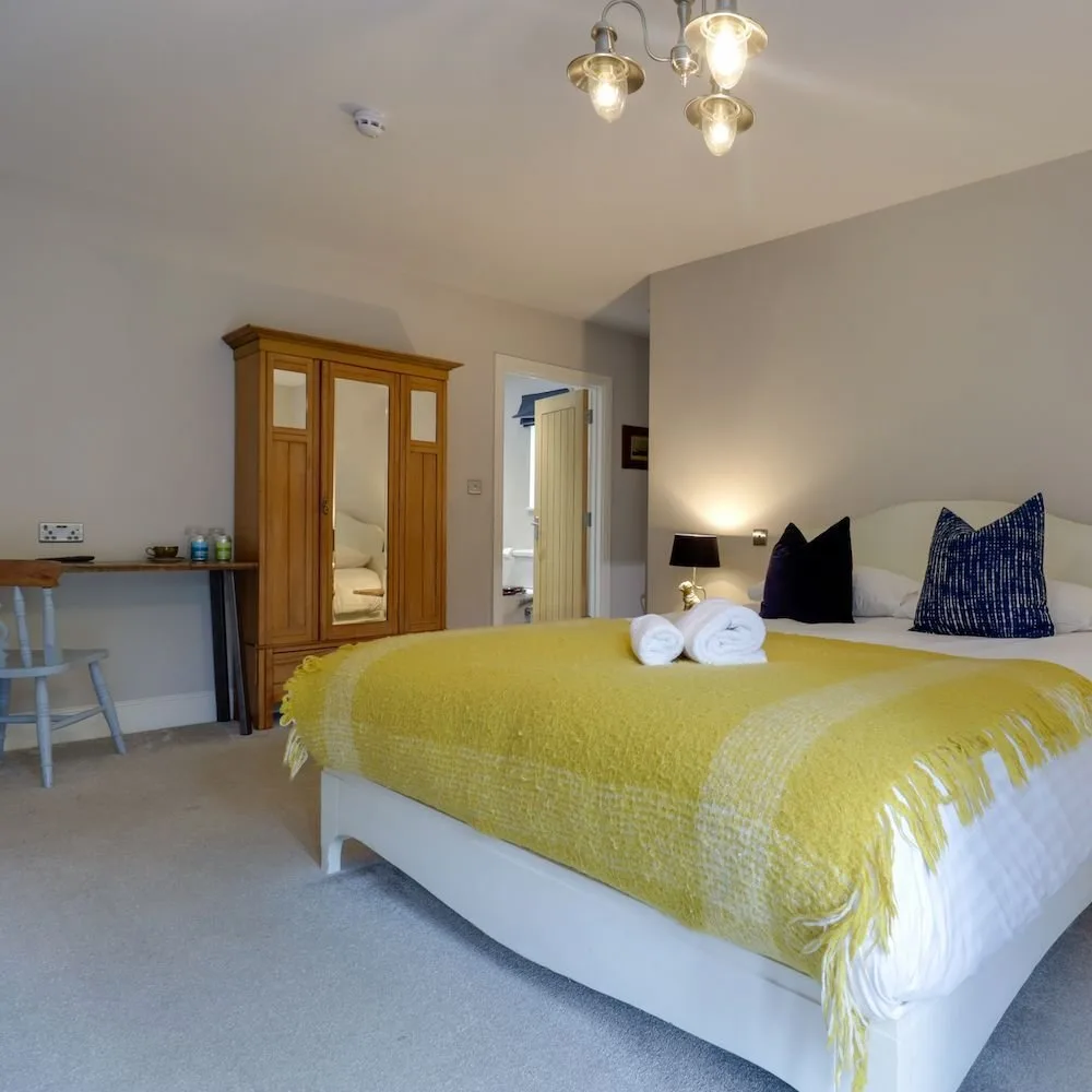 Bedroom with a mustard throw, navy cushions and a small desk beneath the window.
