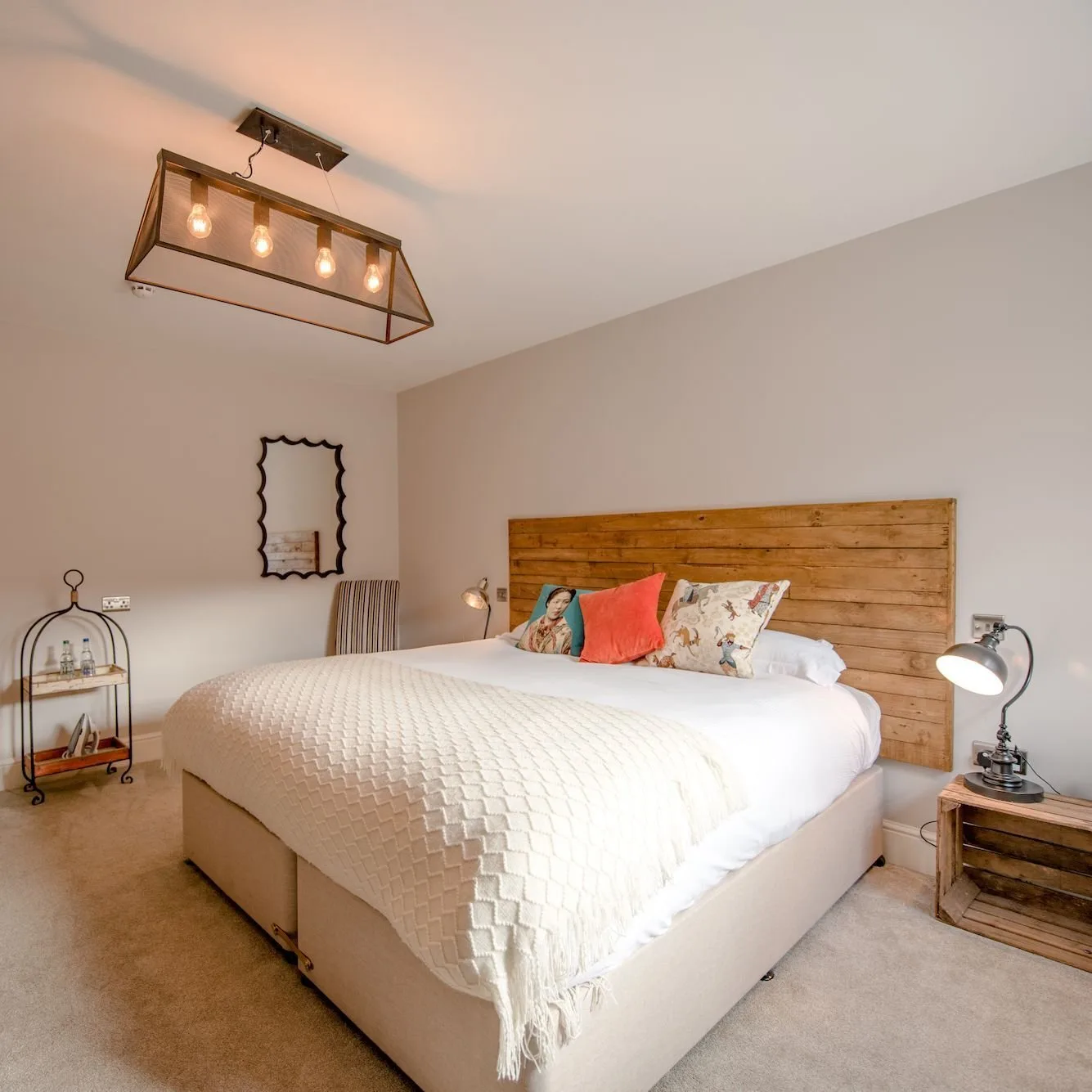 Dormitorio con un cabecero de madera recuperada, un cojín de color coral y una lámpara colgante de estilo industrial.