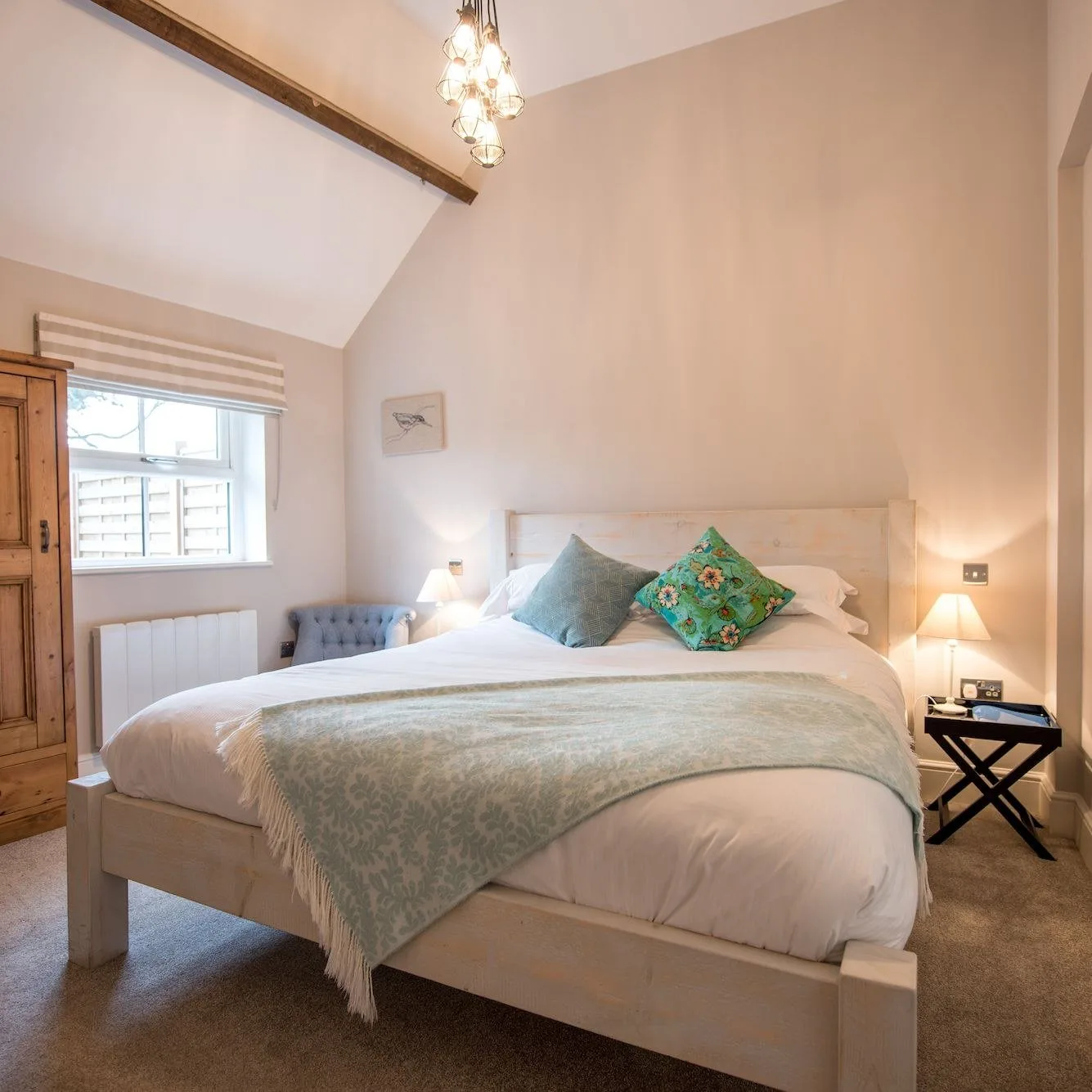 Bedroom beneath a beamed vaulted ceiling, with a whitewashed bed and pine wardrobe.